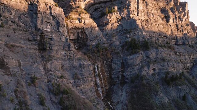 Aerial view of the rugged rock faces and a cascading waterfall in Provo Canyon during golden hour light in Orem, Utah, United States.