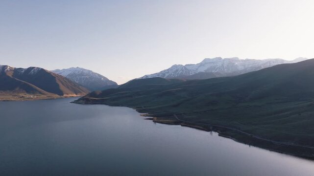 Aerial view of Provo Canyon with snow-capped mountain peaks and a calm lake under a clear sky in Orem, Utah, United States.
