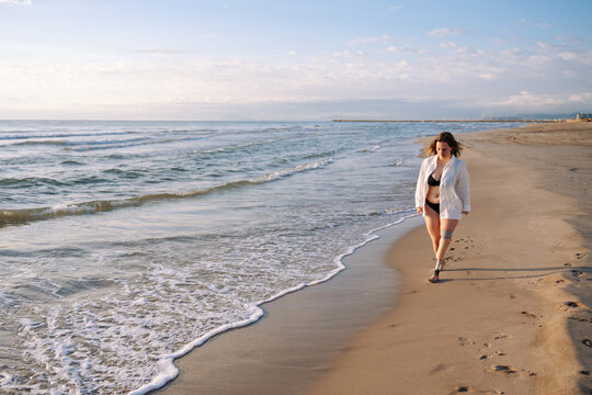 Woman with prosthetic leg walking on beach at sunrise