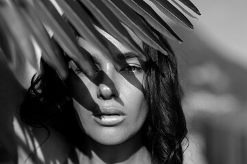 Obraz premium Black and white portrait with palm leaf shadow. Monochrome beauty face with dramatic light and contrast. Closeup woman portrait with strong shadow pattern. Fashion beauty summer face.