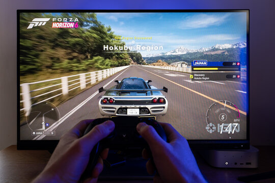 Gamer playing Forza Horizon 6 video game on a computer monitor using a wireless gamepad controller, racing gameplay simulation with red sports car on screen at a desktop setup