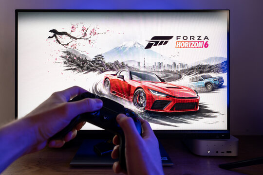 Gamer playing Forza Horizon 6 video game on a computer monitor using a wireless gamepad controller, racing gameplay simulation with red sports car on screen at a desktop setup