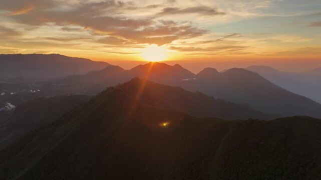 Aerial view of the sun setting behind the mountain peaks of Dieng with a golden sky and soft clouds in Kejajar, Central Java, Indonesia.