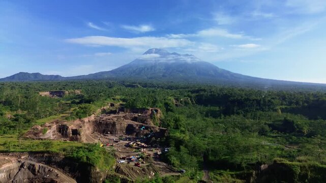 4K aerial footage of Mount Merapi with eroded cliffs and ravines caused by micro-mining in the foreground. A drone view shows green areas and eroded cliffs with the volcano in the background.