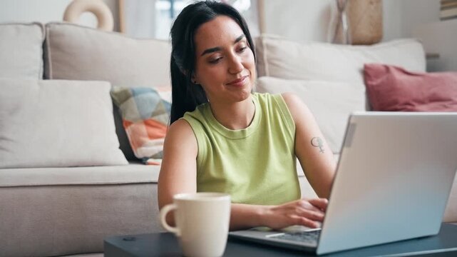 Video of smiling woman working with laptop while drinking coffee  sitting on the floor at home