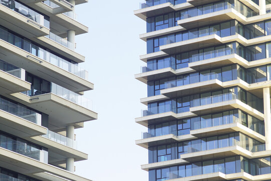 Close-up of two glass-balcony residential towers facing each other across narrow sky gap. Conveys vertical urban density, speculative apartment development, and contemporary city expansion.