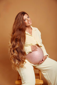 Pregnancy. Smiling pregnant woman touchin tummy isoalted on yellow studio background. Beautiful woman with long wavy hair happy and enjoy with her belly.