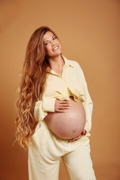 Pregnancy. Smiling pregnant woman touchin tummy isoalted on yellow studio background. Beautiful woman with long wavy hair happy and enjoy with her belly.