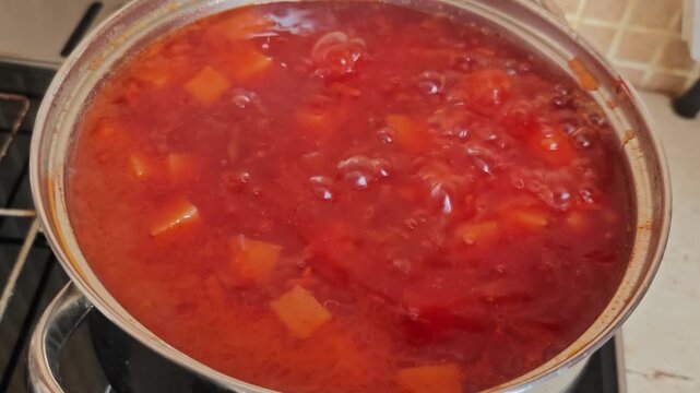 Cooking beetroot borscht at home with bubbling soup in a stainless steel pot on a stove, showcasing vibrant colors and visible ingredients in a cozy kitchen setting