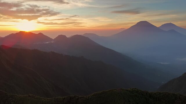 Aerial view of Dieng mountains and volcanic peaks during a golden sunrise with hazy silhouettes in Kejajar, Central Java, Indonesia.