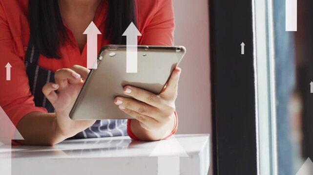 Upward arrows appearing across frame, woman in apron tapping tablet at cafe counter, showing growth