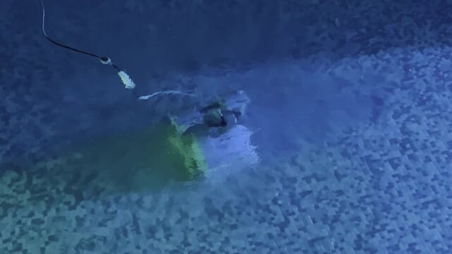 Robotic pool cleaner stops on mosaic pool floor and releases bubbles while cleaning underwater in blue illuminated swimming pool. High quality 4k footage