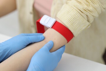 Obraz premium Nurse palpating patient's vein before drawing blood sample at white table in clinic, closeup
