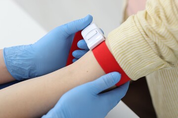 Obraz premium Nurse putting medical tourniquet on patient's arm in clinic, closeup