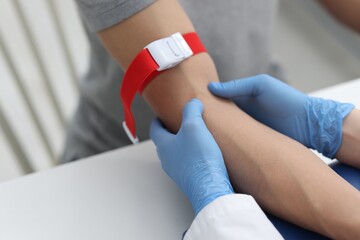 Obraz premium Nurse palpating patient's vein before drawing blood sample at table in clinic, closeup