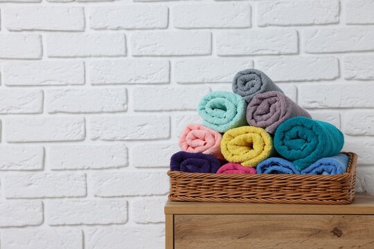 Different colorful towels in basket on wooden cabinet near white brick wall indoors, space for text