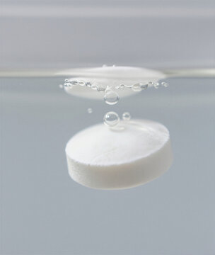 Solid white toothpaste tablet fizzing with micro-bubbles in clear water