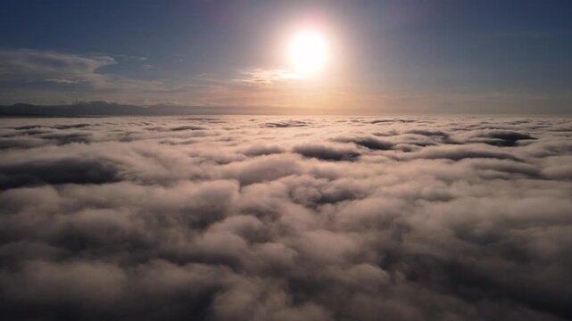 Aerial view of a thick sea of clouds with the bright sun shining in a clear blue sky above the landscape, Purwokerto, Jawa Tengah, Indonesia.