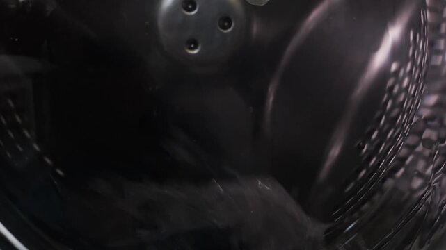 The washing machine is washing clothes, the drum with water and detergent is rotating. Medium shot.