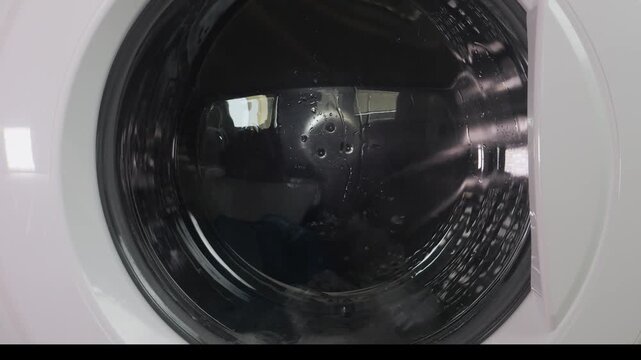 Clothes are washed in a washing machine, the drum with water and detergent is rotating. Medium shot.