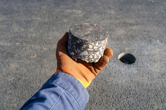 Road worker holding drilled asphalt core sample during pavement inspection and quality control testing on construction site