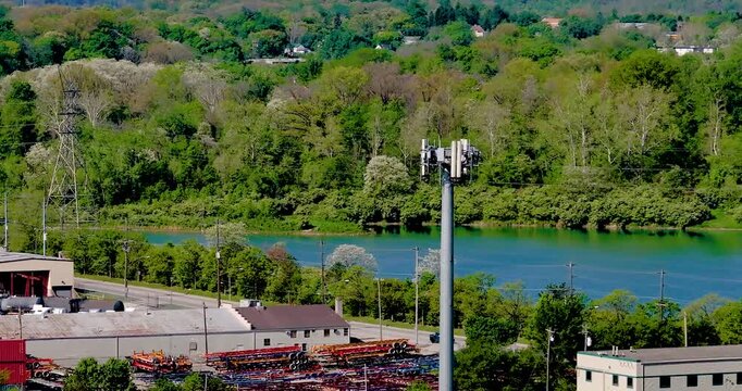 Aerial view of a telecommunications tower standing above industrial buildings and a river with lush green hills in the background in Cincinnati, Ohio, United States.