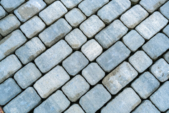 Closeup of gray cobblestone pavement laid in diagonal pattern, textured stone blocks background