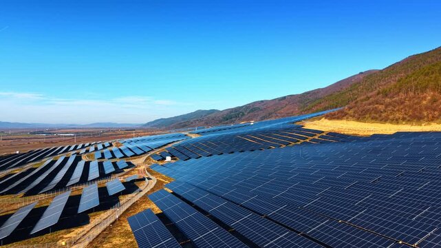 Photovoltaic cell fields at the mountain foot. Bright sun lights the wild nature landscape at sunset. Aerial view.