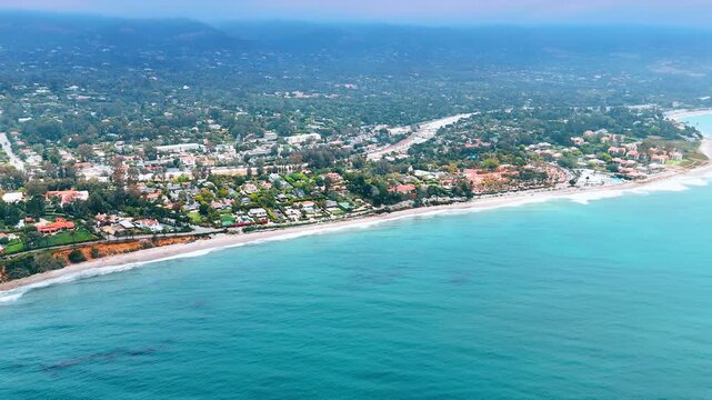 Flight above the blue waterscape approaching the green shore. Beautiful coast of the Pacific Ocean in Santa Barbara, California, USA.