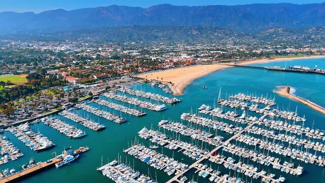 Multiple modern boats at the berths in the yacht club. Panorama of picturesque Santa Barbara, California, USA surrounded by mountains in the backdrop. Aerial view.