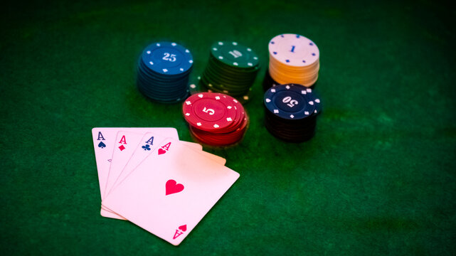 Four aces playing cards with colorful poker chips on green felt table background