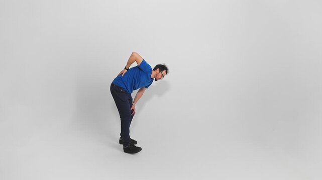 Isolated view of unhealthy man walking bent holding back and knee by hands filmed in studio. Uncomfortable movement of young adult guy caused by chronic backache and spinal problems. Rheumatism theme.