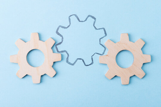 Missing link business concept or HR with wooden gears and a hand drawn outline on a blue background.