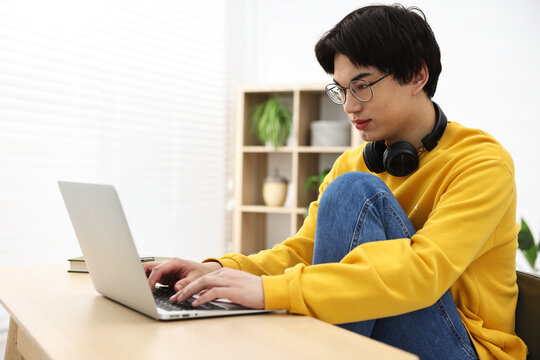 Young student studying with laptop at wooden table indoors