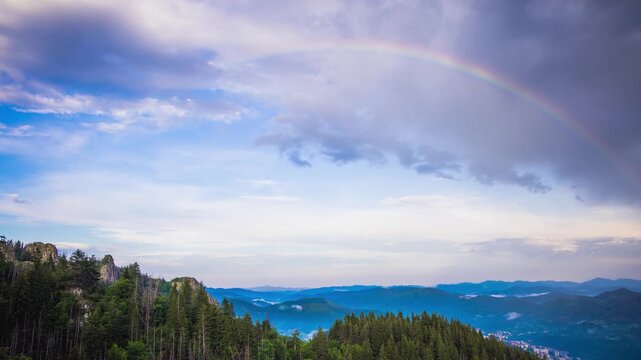 Multi-colored rainbow flaunts on top of the Rhodope Mountains above intermountain valley with the village of Smolyan