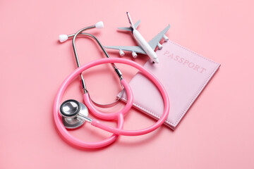 Fototapeta premium Medical tourism. Passport, stethoscope and plane model on pink background, closeup