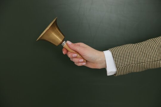 School holidays. Teacher ringing golden bell near chalkboard, closeup