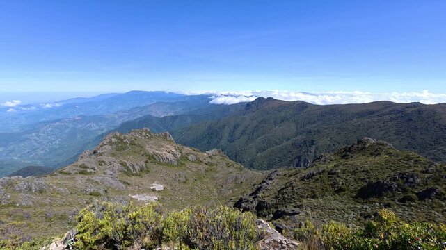 Breathtaking panoramic panning shot above Cerro Ventisqueros in Chirripo National Park, Costa Rica. White clouds rest on mountain peaks under a brilliant clear blue sky on a sunny day.