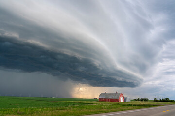 Dramatic shelf cloud looms over a red barn and green fields under a stormy sky © pictureguy32
