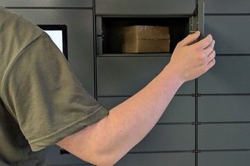 Obraz premium man places a package into a parcel locker. Modern automated locker. no face