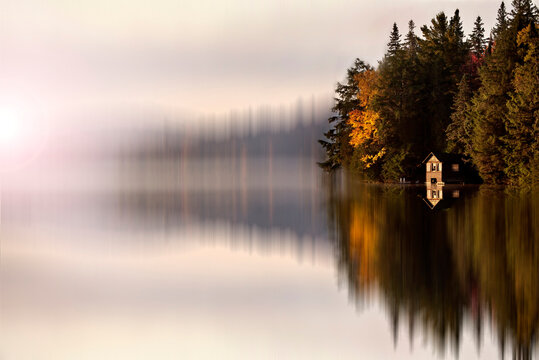 Serene cabin nestled among autumn trees reflected in a misty lake
