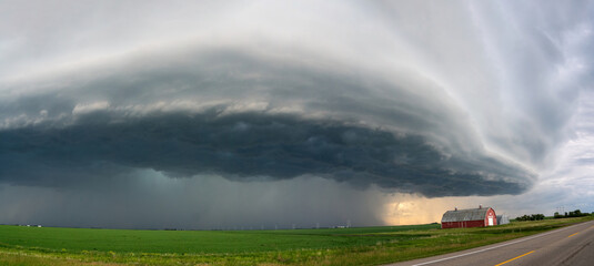 Fototapeta premium Massive supercell thunderstorm looms over a rural landscape with a red barn