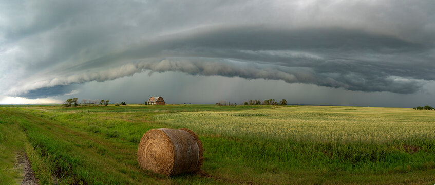 Dramatic storm clouds loom over a rural landscape with a barn and hay bale