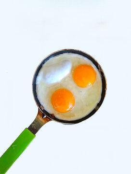 close up view of delicious food. two chicken eggs, yolks and whites in a small aluminum frying pan with a green handle  on a white background
