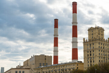 Fototapeta premium Industrial Skyline With Twin Smokestacks Looming Above Soviet Apartment Blocks Beneath Heavy Clouds, Faint Smoke Plumes Drifting, Muted Tones,