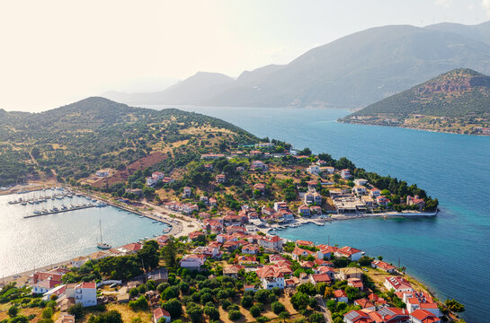 Vathy village buildings with terracotta roofs spread across the hillsides. Overlooking the calm bay with yachts moored in a bustling marina. Surrounded by green mountains and the sparkling ionian sea
