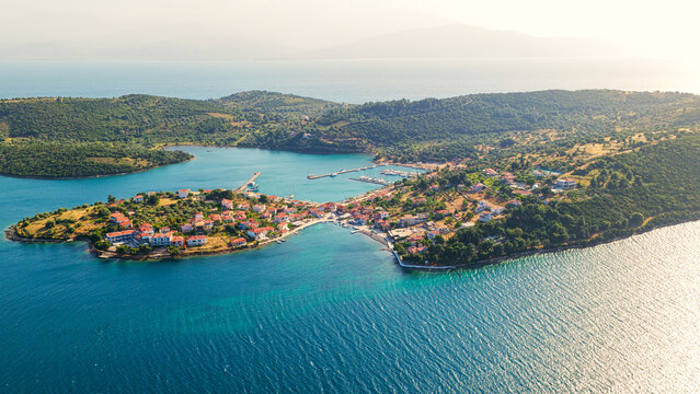 Trikeri island village featuring traditional houses with red rooftops, a lively marina with boats, and lush green hills surrounded by the clear turquoise waters of the sea