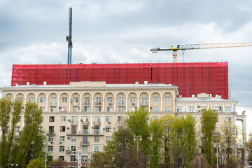 Historic Facade With Red Scaffolding Wrap Showing Upperlevel Renovation, Cranes Lifting Materials, Protective Tarpaulin Covering Upper Stories, Ornate © Egor Lint