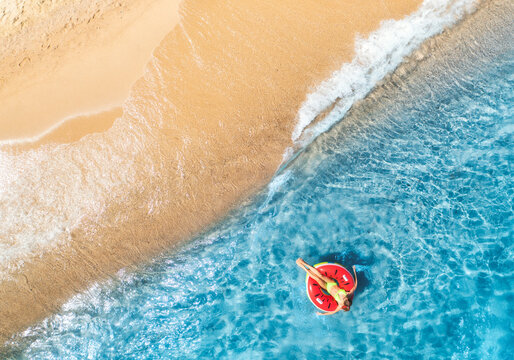 Aerial view of a young woman swimming with red swim ring in blue sea with waves in summer. Tropical landscape with girl, clear water, sandy beach. Top down view. Vacation. Sardinia island, Italy