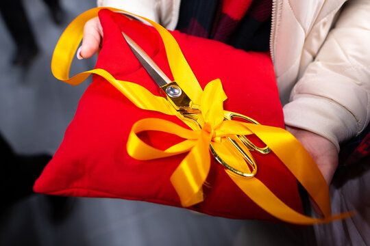 Large ceremonial scissors tied with ribbon placed on a red cushion. Grand opening and ribbon cutting ceremony concept.